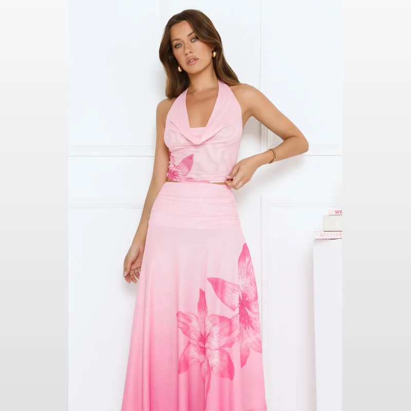 Woman wearing a pink halter neck crop top with a floral print and cowl neckline, paired with a matching pink floral print maxi skirt.