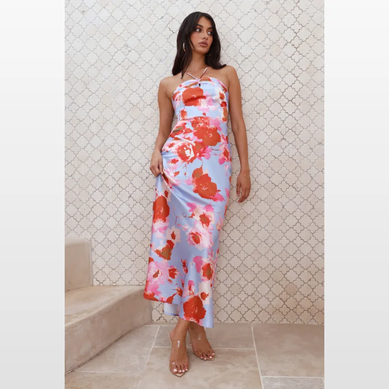 Woman wearing a blue satin maxi dress with a bold red and pink floral print, featuring a halter neckline and a flowy skirt.