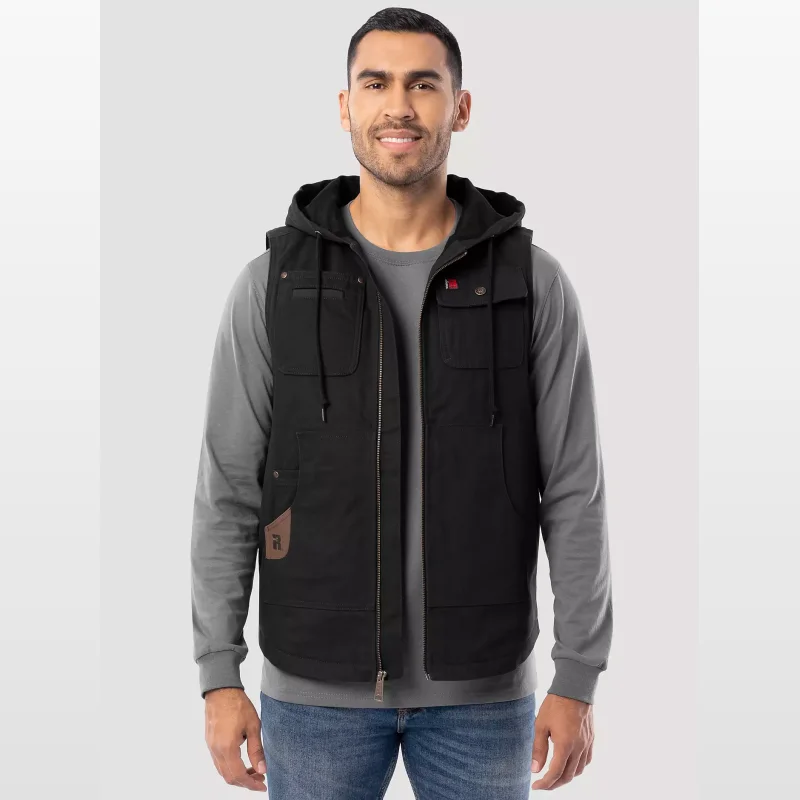 Man wearing a black Wrangler RIGGS WORKWEAR® hooded work vest over a grey long-sleeved shirt and blue jeans.