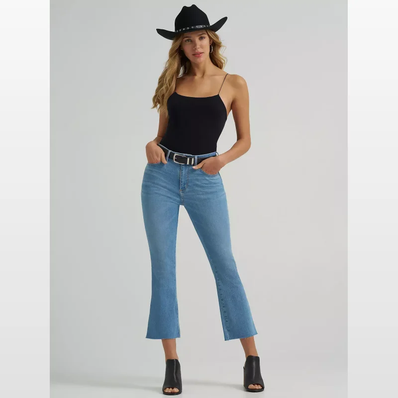 Woman wearing light blue Wrangler Bespoke Kick Flare Jeans with a raw hem, a black camisole, a black cowboy hat, and black heeled boots.