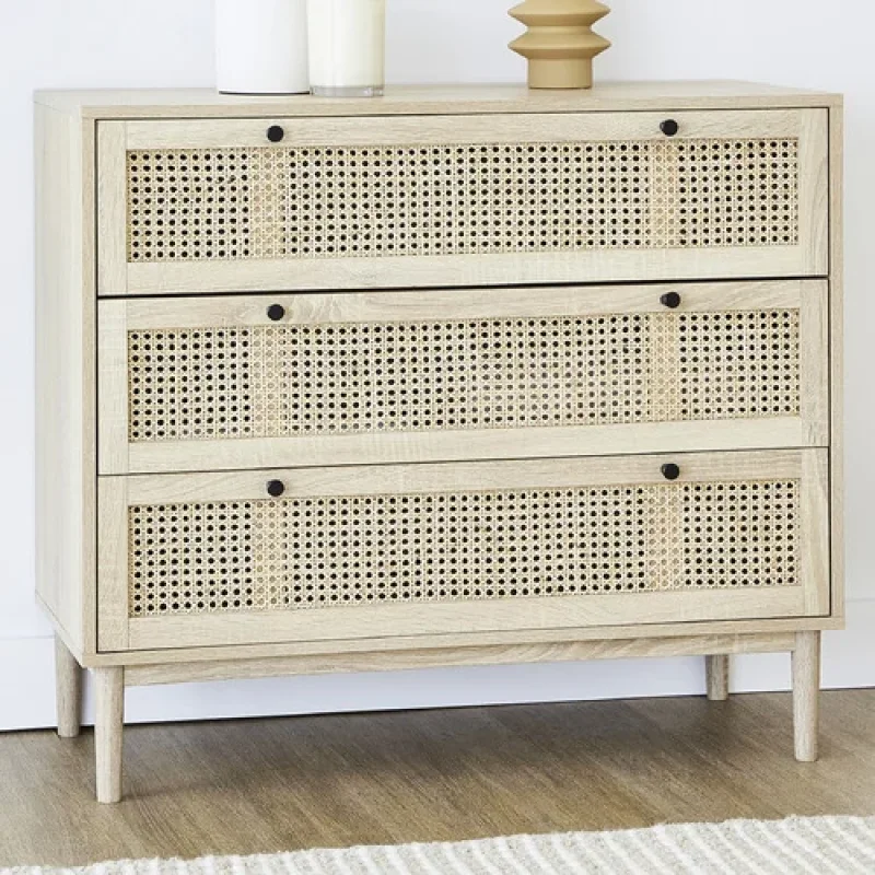 A light wood three-drawer chest with cane detailing on each drawer front and black knobs, set on tapered legs.