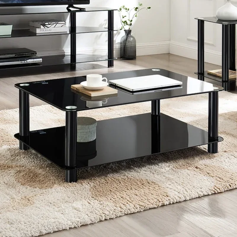 A modern black glass coffee table with two tiers, supported by black cylindrical legs, placed on a textured rug in a living room setting.