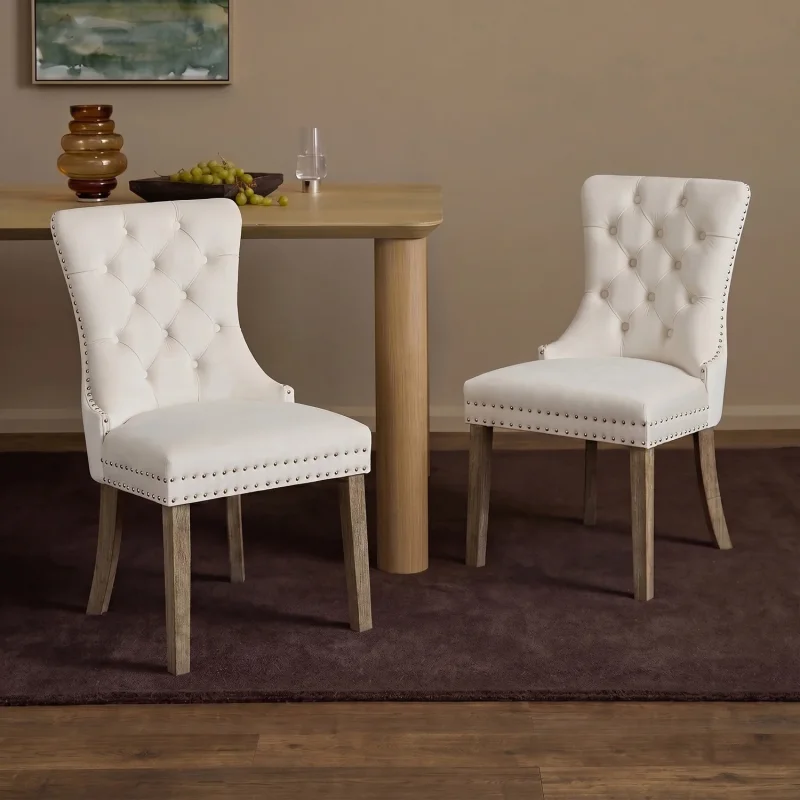 A set of two Aylin velvet dining chairs in off-white with button tufting and nailhead trim, featuring wooden legs.