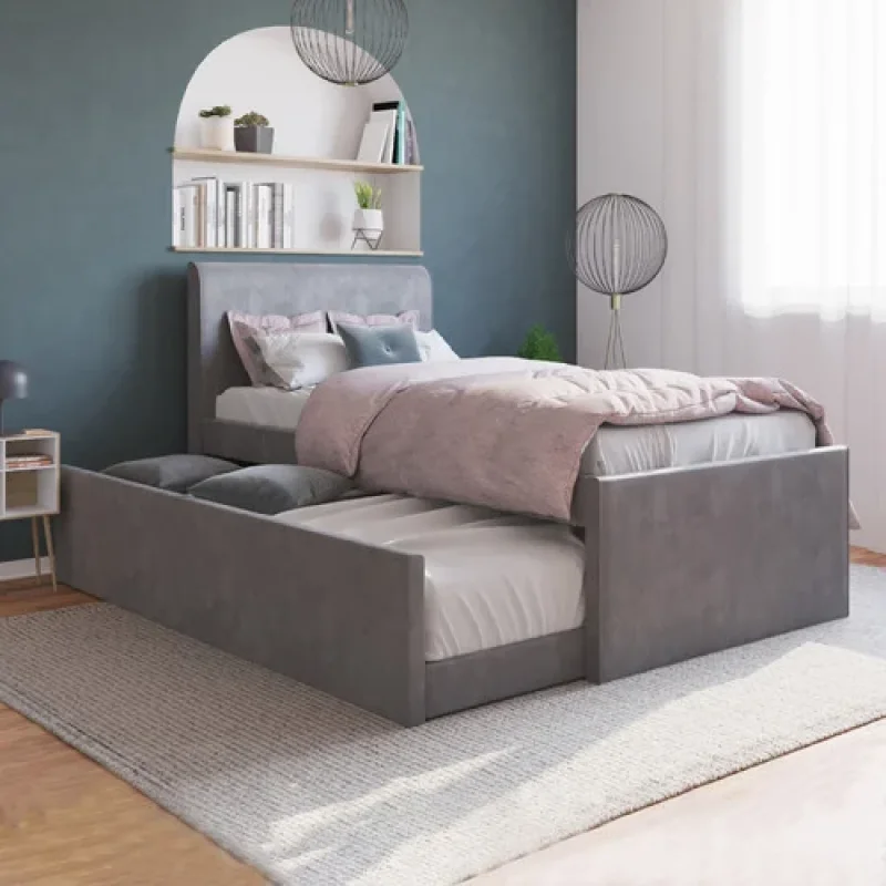 A grey velvet king single bed frame with a trundle bed pulled out, featuring a modern design and upholstered headboard. The bed is made up with pink and white bedding.