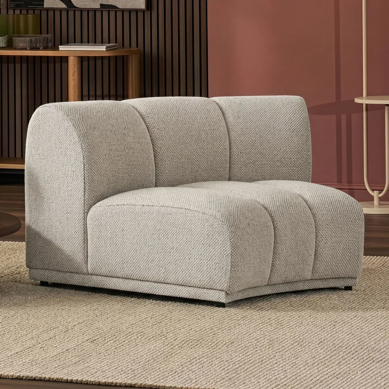 A light beige, textured, armless lounge chair with curved backrests and a low profile, placed on a beige rug in a room with a wooden wall and a terracotta-coloured wall.