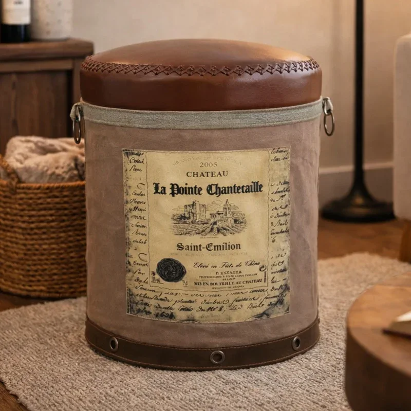 A round Chateau-themed ottoman with a brown leather top and a canvas body featuring a vintage wine label.