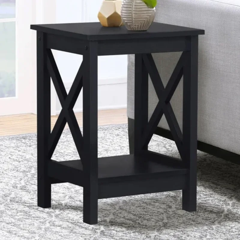 A black wooden Vance side table with an X-frame design and a lower shelf, placed on a rug next to a sofa.