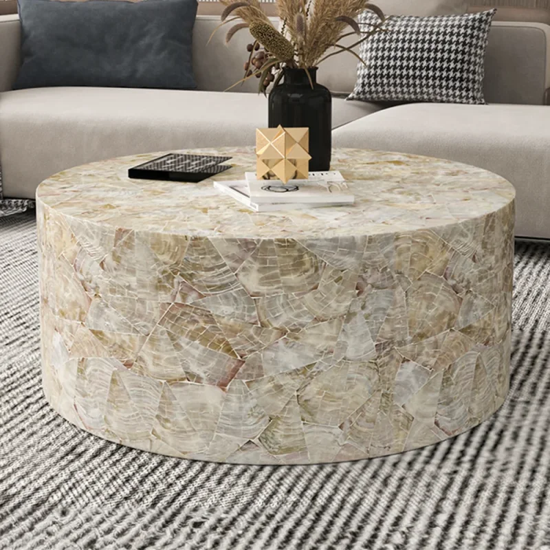 A round coffee table with a unique mosaic pattern made of natural shell pieces, placed in a modern living room setting.