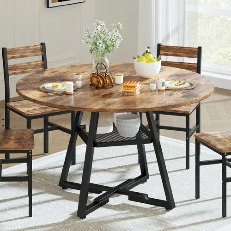 A round wooden dining table with a rustic finish and black metal legs, set with chairs and breakfast items.
