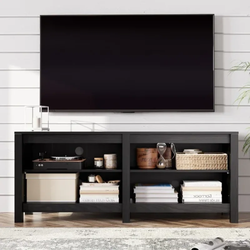 A black, modern TV unit with open shelving, displaying a record player, books, decorative items, and a basket, with a large TV mounted above it.