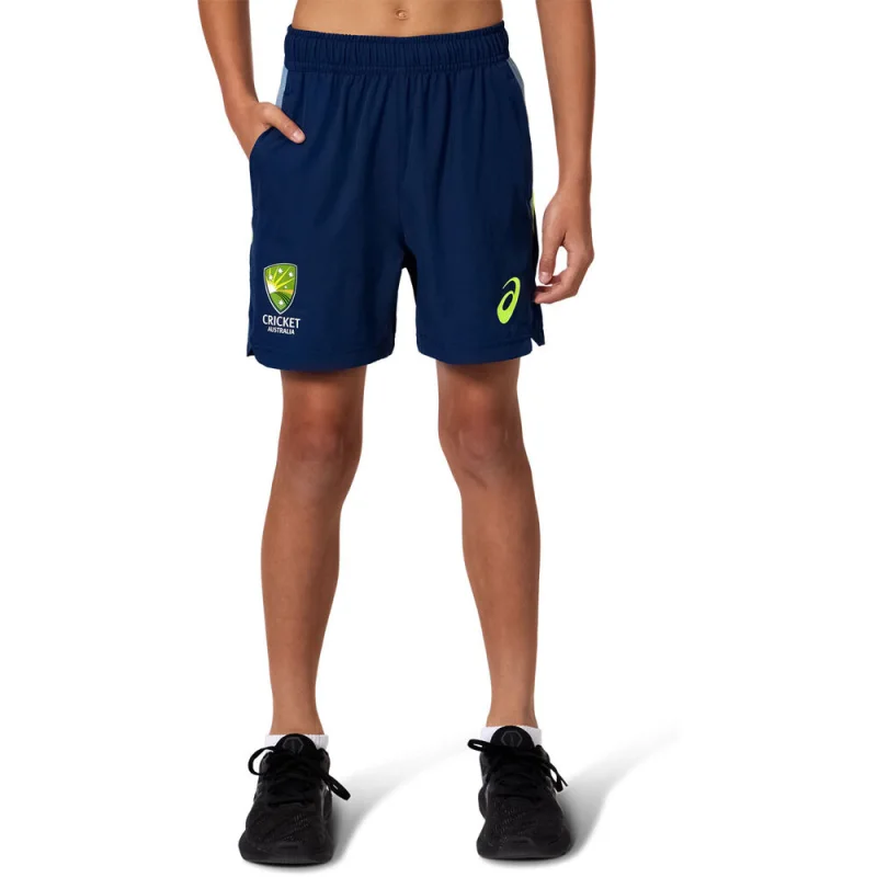 A young person wearing navy blue Cricket Australia 2025/26 kids training shorts with yellow Cricket Australia logo on the left leg and yellow ASICS logo on the right leg.