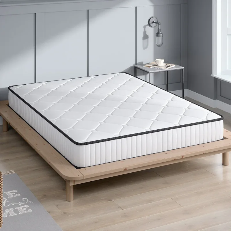 A white Slumber 5 Zone Pocket Spring Mattress with a black trim, shown on a wooden bed frame in a bedroom setting.