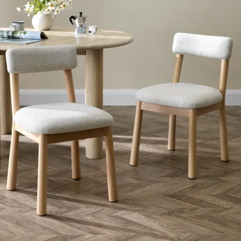 Two upholstered dining chairs with light grey fabric seats and backs, and natural beech wood frames, placed around a wooden dining table.