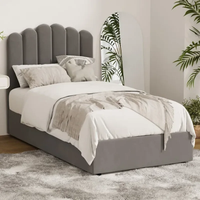 Grey Ellora Velvet Gas Lift Bed Frame with a scalloped headboard and storage base, styled with white bedding and decorative cushions.