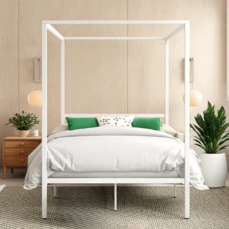 A white metal canopy bed frame with sleek lines, set up in a bedroom with white bedding and green accent pillows.