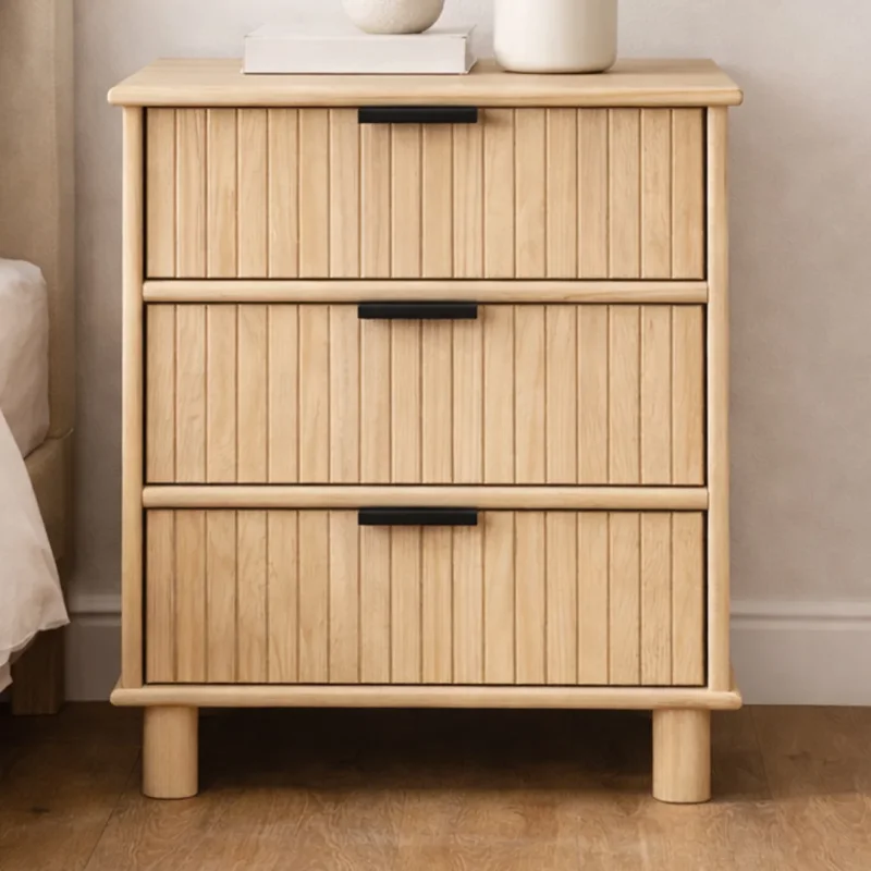 A light wood bedside table with three drawers, each featuring a black handle and a fluted front.