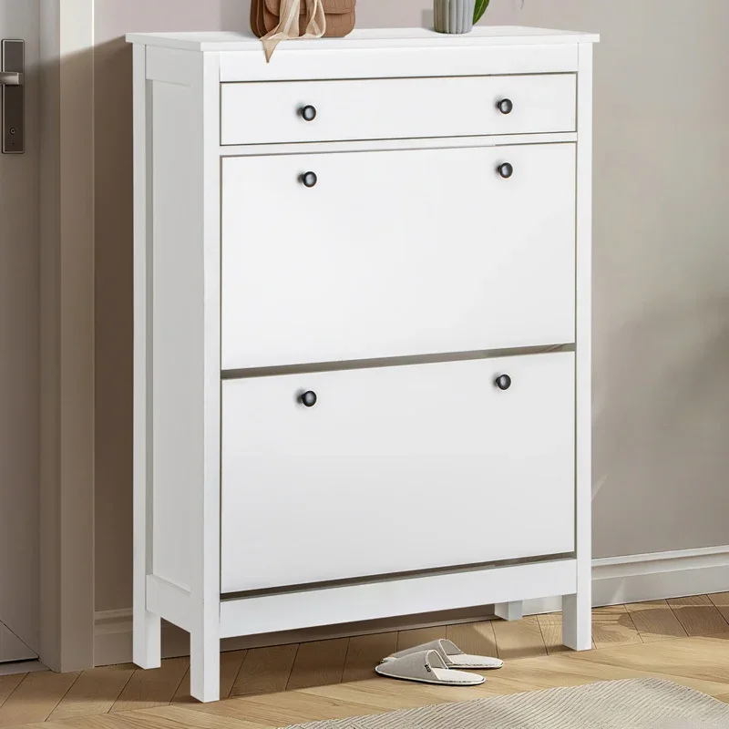 A white Finley 1 drawer shoe cabinet with two flip-down doors, featuring black knobs, placed in a hallway with a door and wall mirror in the background.