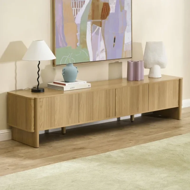 A long, low-profile Walter 4 Door TV Unit made of light-coloured oak wood, featuring four cabinet doors and a minimalist design, placed against a neutral wall with abstract art above.