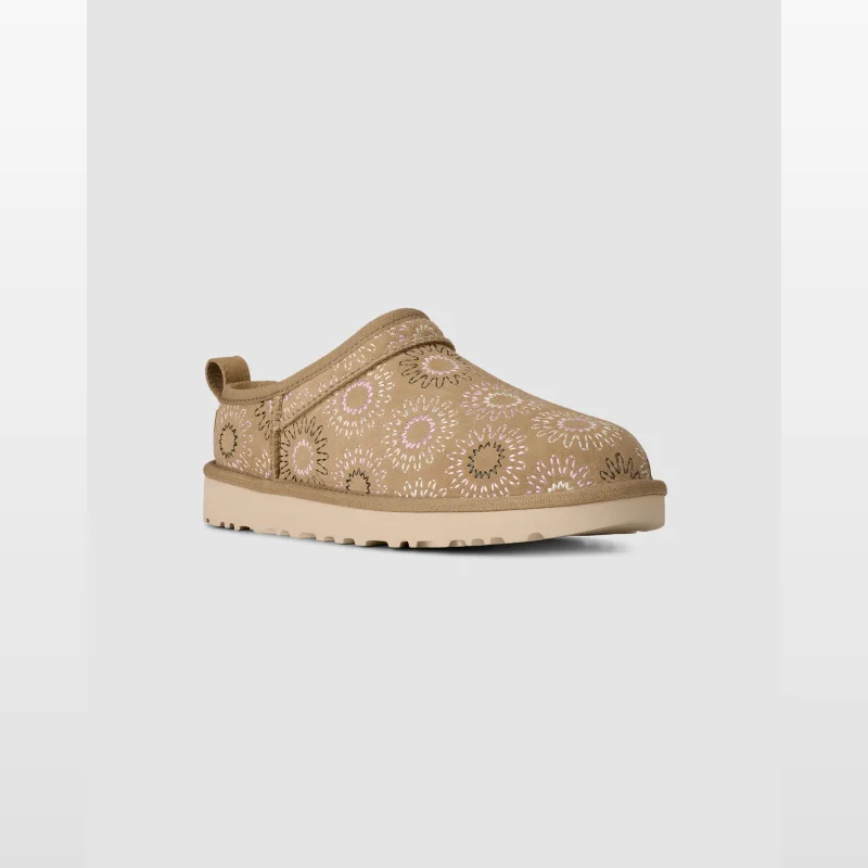 Tan suede clogs with a sunburst embroidery pattern in pink and white, featuring a rear pull tab and a thick beige sole.