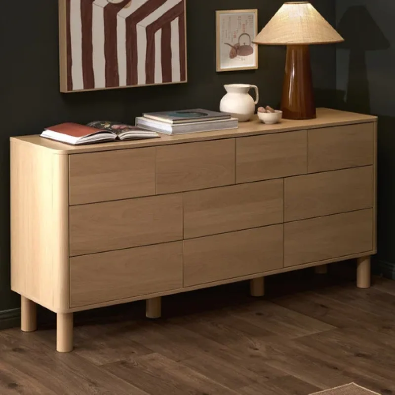 A light oak 10-drawer chest with rounded edges and tapered legs, styled with books and a lamp on top.