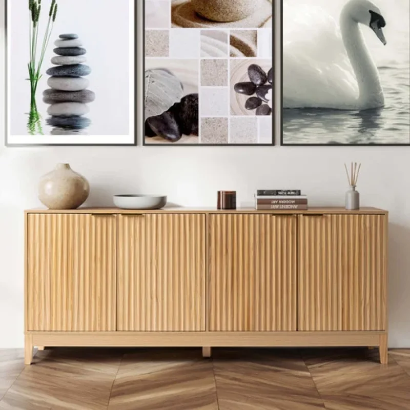 A light wood-toned sideboard buffet with four fluted doors and a low-profile base, set against a white wall with decorative art above.