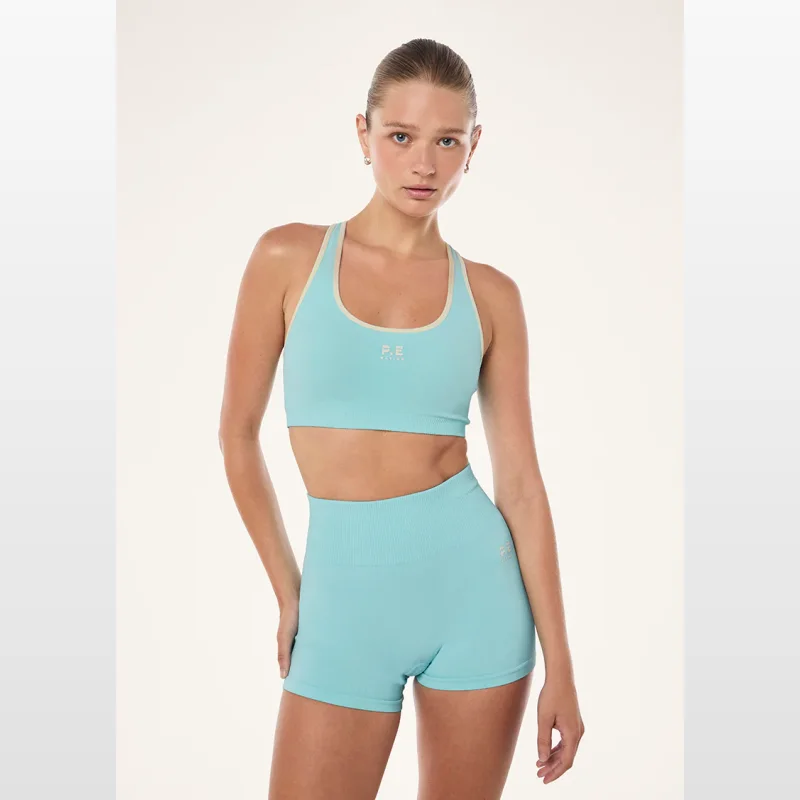 Woman wearing a light blue Pe Nation Adaption Seamless Sports Bra with contrast trim and a matching pair of seamless shorts.