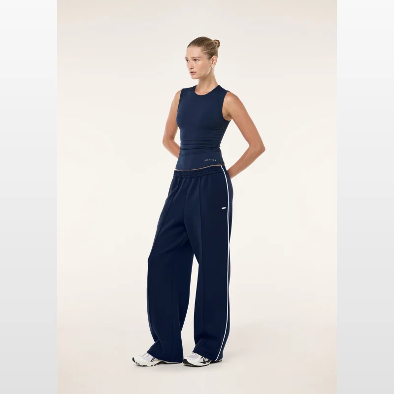 Model wearing Pe-nation Triumph Pant in Dark Navy, a mid-rise relaxed fit pant with white contrast piping and a silver branded badge.