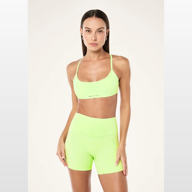 Woman wearing a neon lime green Pe-nation sports bra with thin adjustable straps and a low scoop neckline.