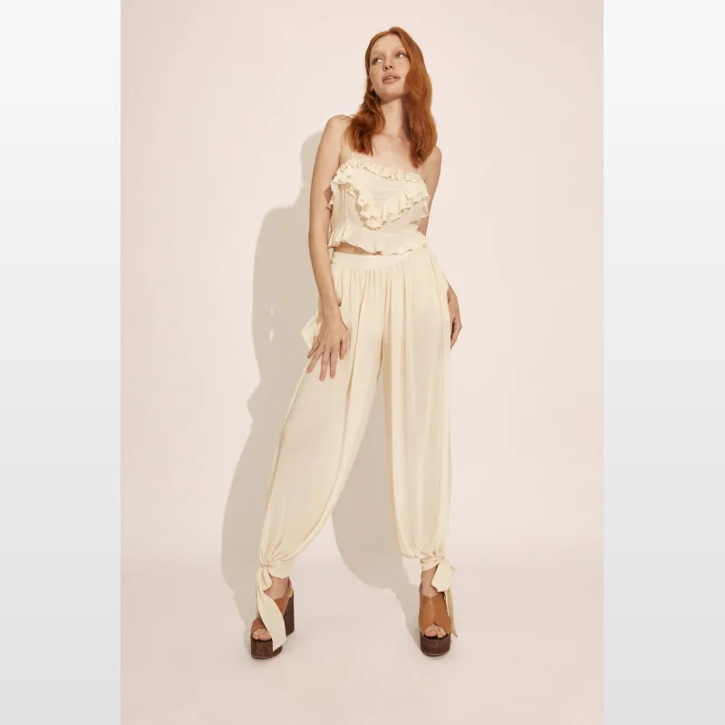 Model wearing a soft beige Bardot Alira Frill Detail Crop Top with adjustable straps and a straight neckline, featuring frill detailing along the neckline and a button back closure.