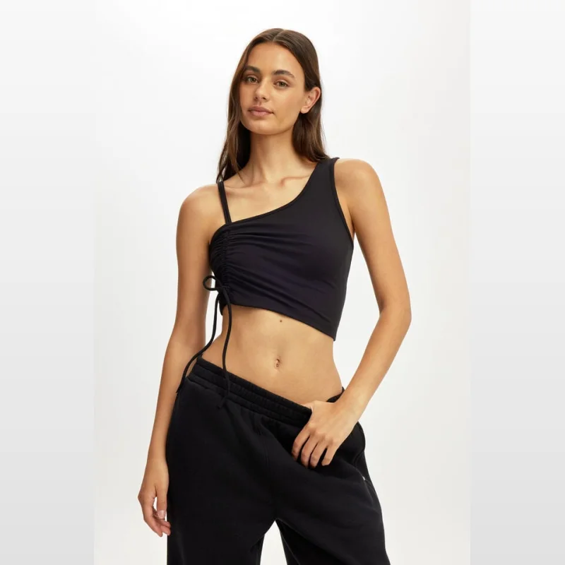 Woman wearing a black, ultra-soft, asymmetric side gather tank top with a drawstring detail and a single strap on one side and double straps on the other.