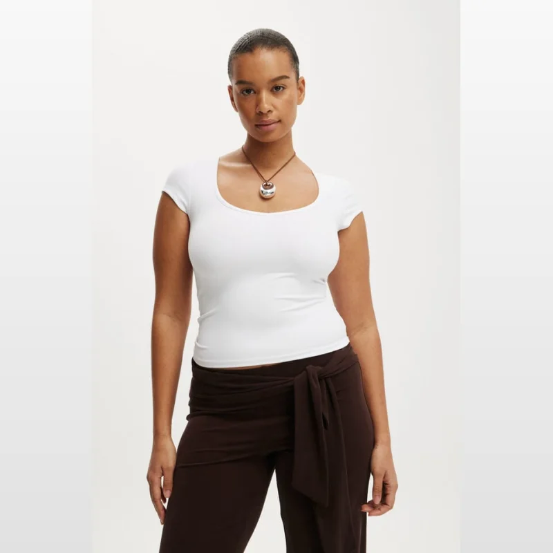 Woman wearing a white short-sleeve V-neck fitted top and brown wrap-around pants.
