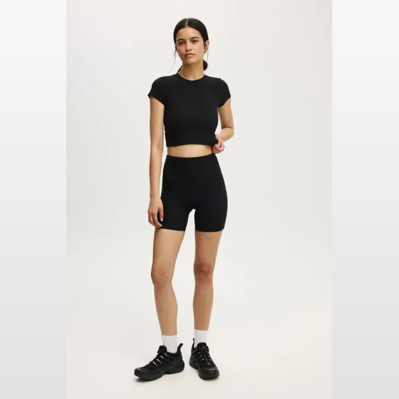 Woman wearing black Cottonon Ultra Soft Rib Bike Shorts and a matching crop top, standing against a white background.