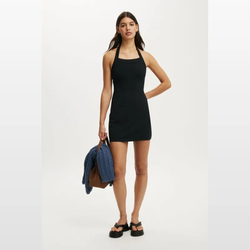 Woman wearing a black Hailey Halter Mini Dress by Cottonon, holding a blue knit cardigan and a brown bag.