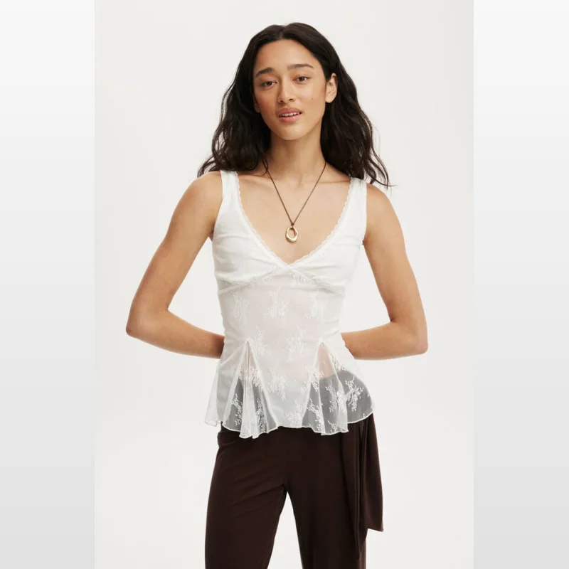 Woman wearing a white Elsie Babydoll Tank top with lace trim and a V-neckline, featuring a textured floral design and mesh lining.