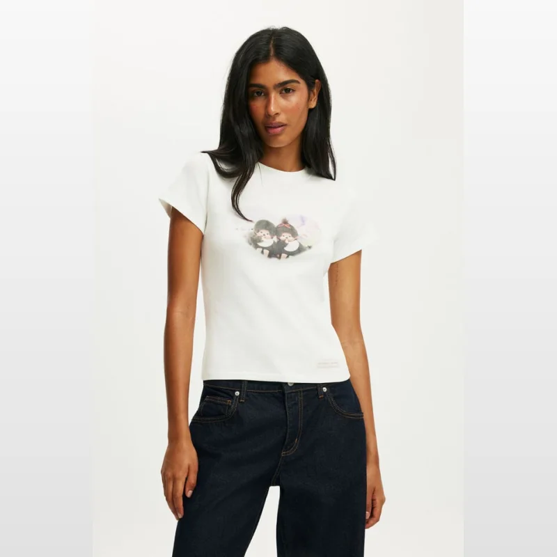 Woman wearing a white Cottonon Monchhichi graphic tiny tee with a round neck and short sleeves, paired with dark wash jeans.