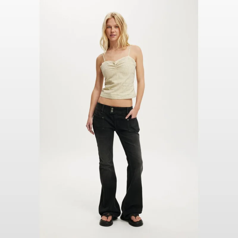 Woman wearing a yellow and white gingham check cotton cami top with a bow detail and adjustable straps, paired with dark wash flared jeans.