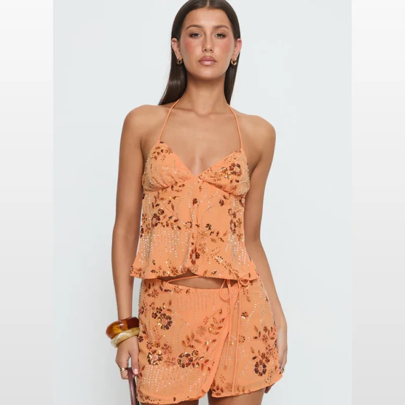 Woman wearing an orange beaded halter neck top with a V-neckline, ruched bust, and tie-back detail. The top features a floral and sequin embellishment.