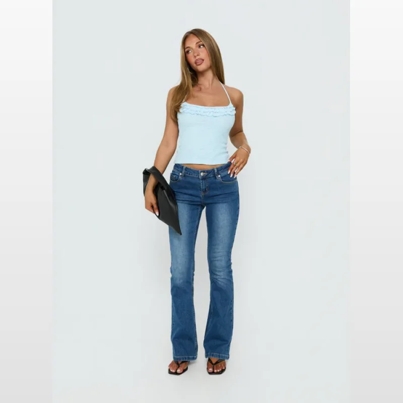Woman wearing a light blue knit halter top with ruffle detail around the neckline and a low back, paired with blue flare jeans.