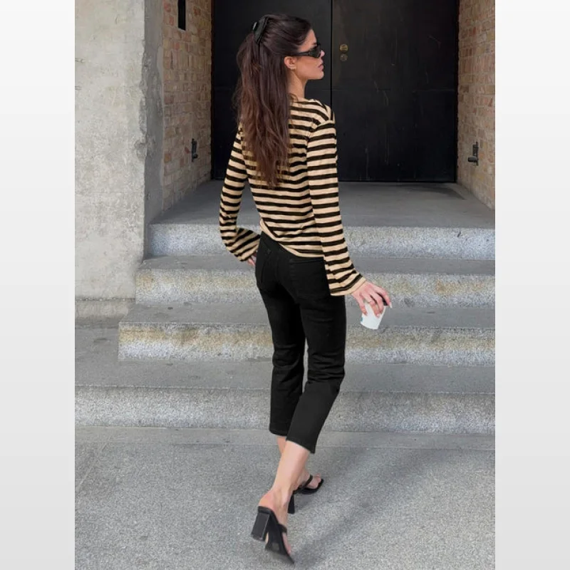 Woman wearing high-rise, cropped black jeans and a striped long-sleeved top, walking down stairs.