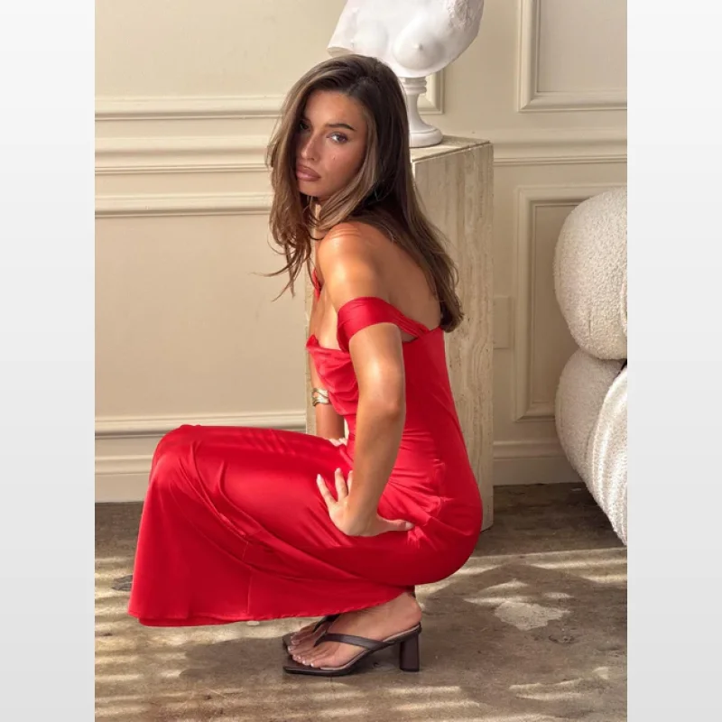 Woman wearing a red off-the-shoulder satin maxi dress, crouching on the floor.