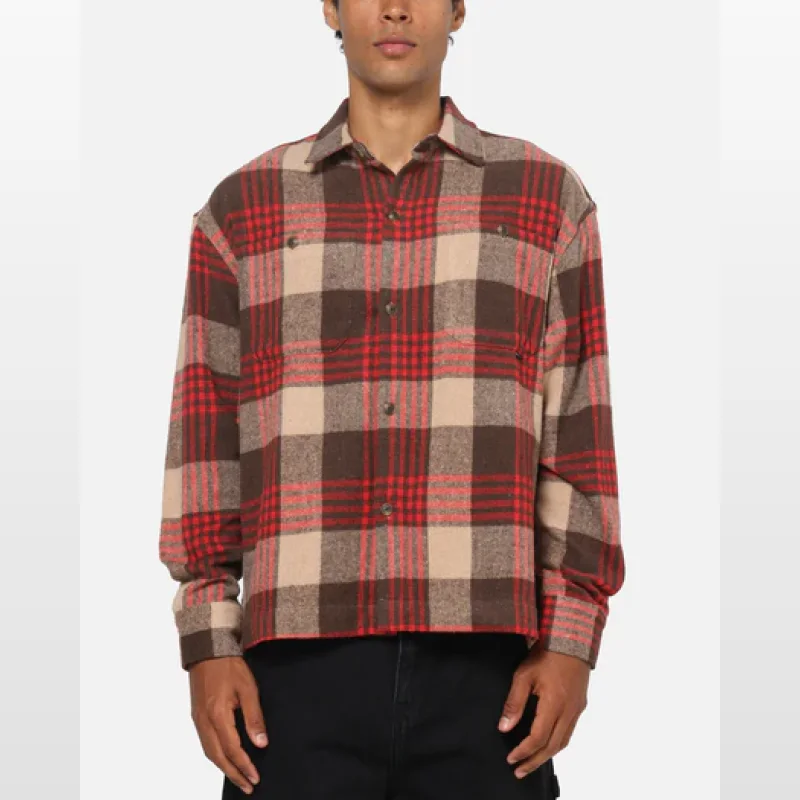Man wearing a brown, red, and beige plaid flannel shirt with chest pockets and button-up cuffs.