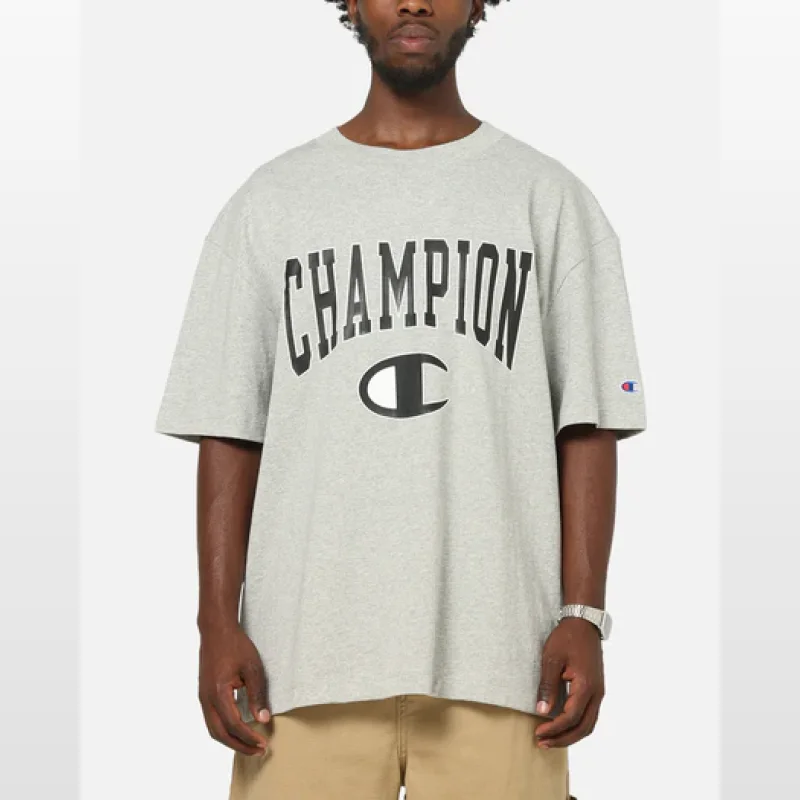 Man wearing a grey marle Champion athletic t-shirt with a large black 'CHAMPION' graphic across the chest and a smaller Champion 'C' logo on the sleeve.