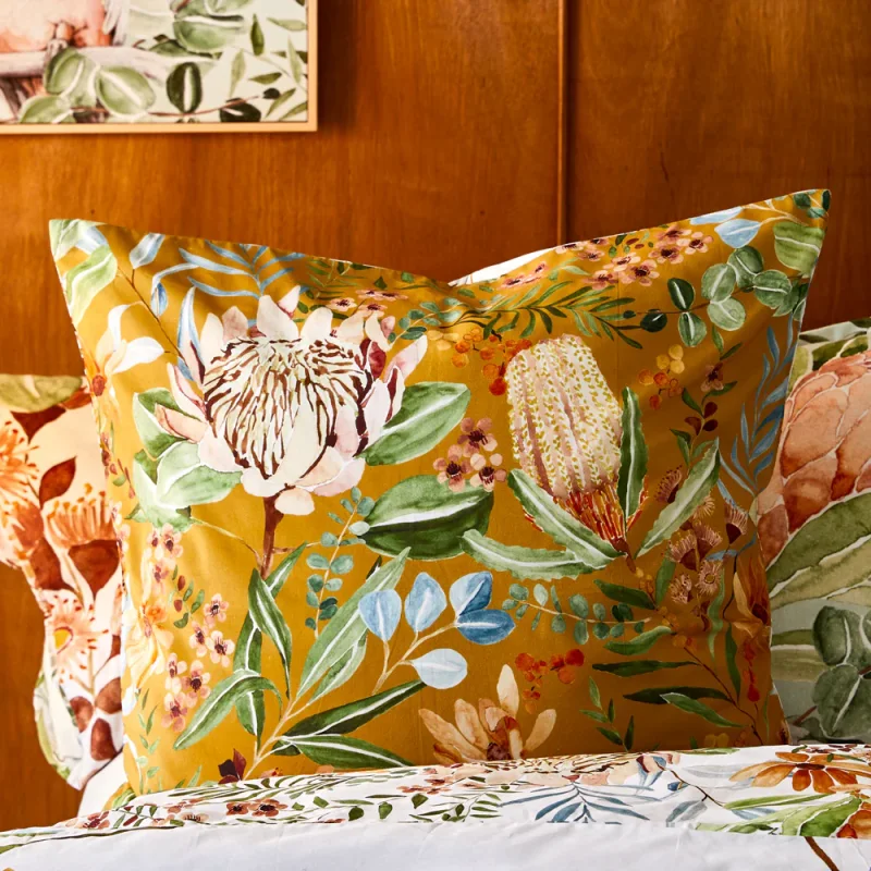 A close-up of a MyHouse Darwin European Pillowcase featuring a hand-painted design of native Australian flora, including proteas and banksias, on an ochre background.