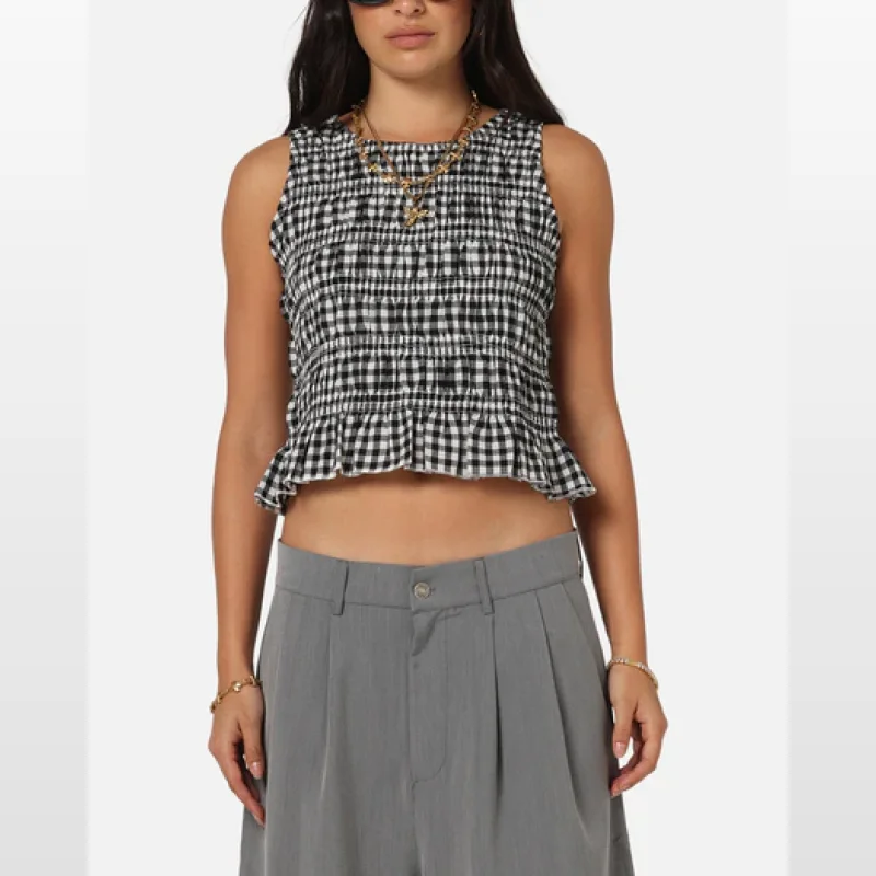 Woman wearing a black and white check shirred sleeveless top with a frill hem and a ribbed neckline.
