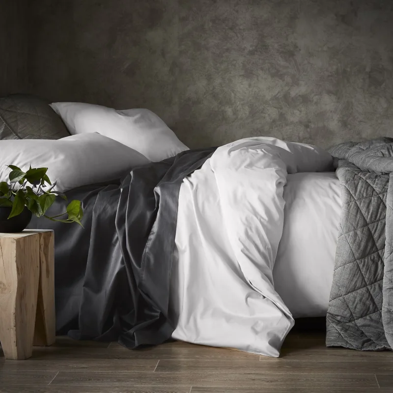 A neatly made bed with white European pillowcases and a dark grey duvet cover, set against a textured grey wall.
