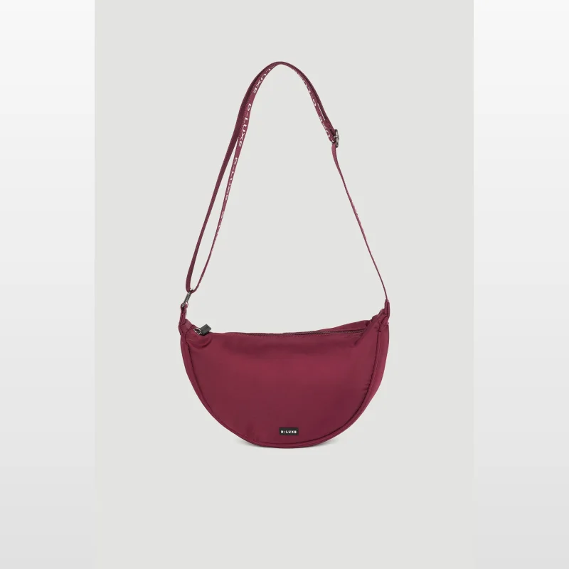 A burgundy D-Luxe half moon crossbody bag with an adjustable strap featuring repeating D-Luxe branding, set against a plain grey background.