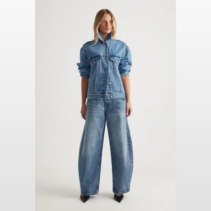 Woman wearing Decjuba Daisy Horseshoe Jeans in a light blue wash, featuring a high rise, wide leg that curves out at the hip and tapers slightly at the ankle.