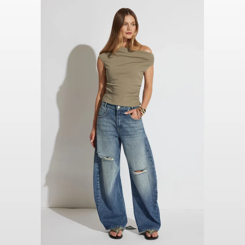 Woman wearing a fitted olive green tipped shoulder top with an asymmetrical off-shoulder neckline and short sleeves, paired with distressed wide-leg jeans.