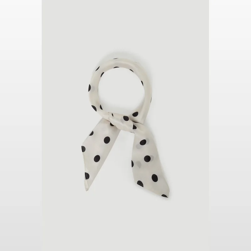 A cream-coloured scarf with black polka dots, tied in a knot.