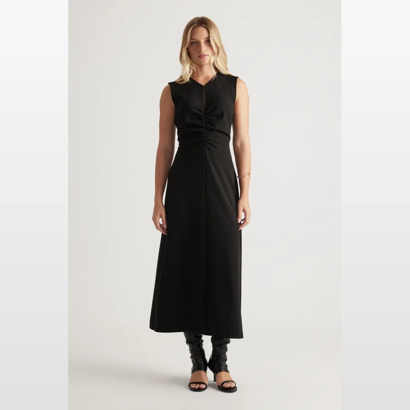 Woman wearing a black sleeveless midi dress with ruched detailing on the front and a high round neckline.